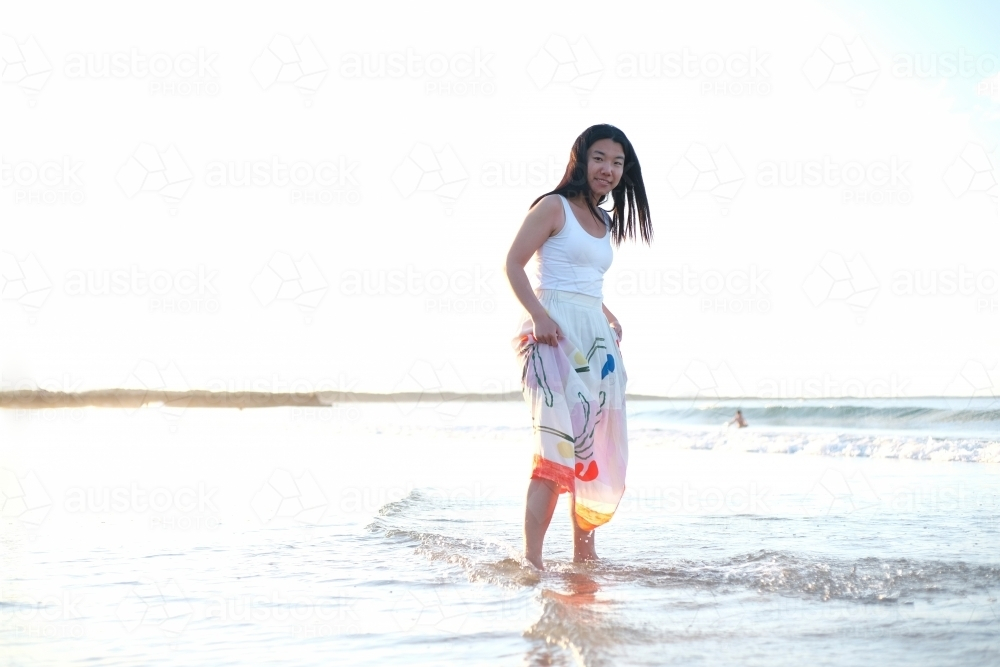 Asian woman walking along the beach while holding her skirt up - Australian Stock Image