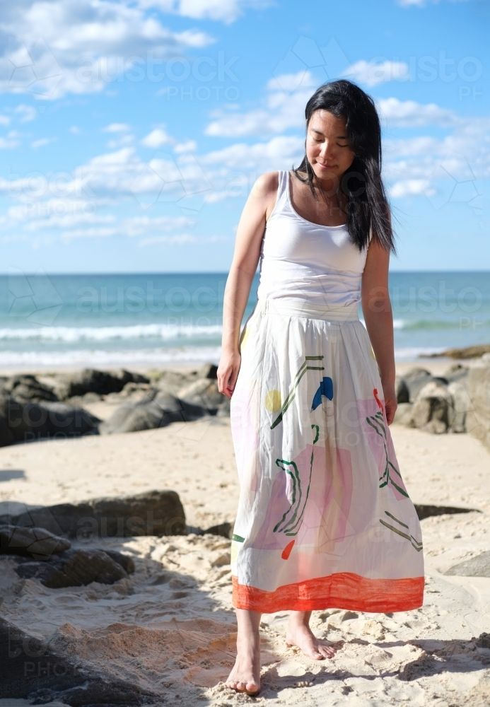 Asian woman wearing a long white skirt on the beach - Australian Stock Image