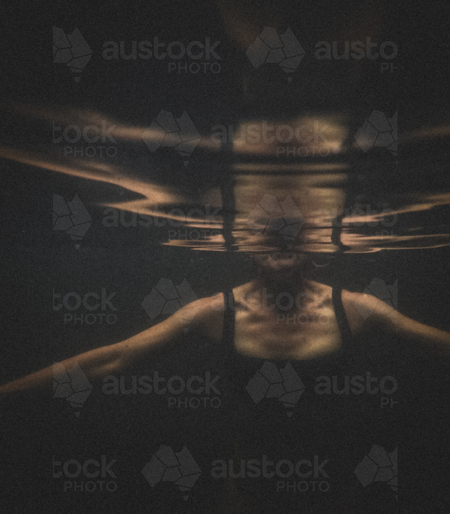 Athletic Upper female torso in black bathers underwater with reflection - Australian Stock Image