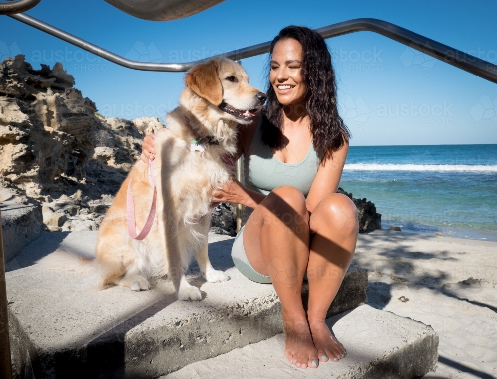 Image of Athletic woman in gym wear sitting with golden dog on beach ...