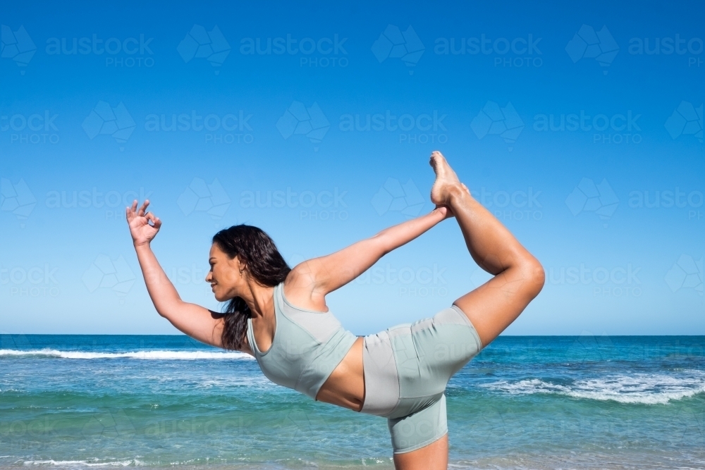 Athletic woman in standing yoga pose with ocean in background - Australian Stock Image