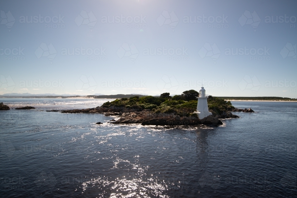 Attractive little navigational lighthouse on a rocky island, blue water, blue sky with flare - Australian Stock Image