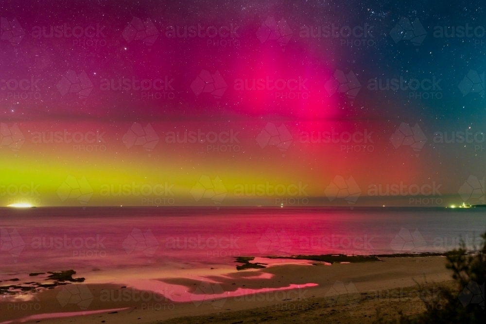 Aurora Australia illuminating the night sky over an ocean bay - Australian Stock Image
