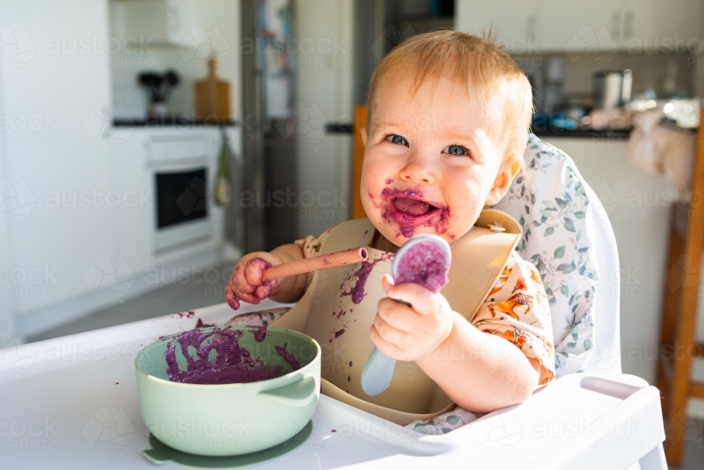 Aussie baby eating food in highchair - purple smoothie breakfast - Australian Stock Image