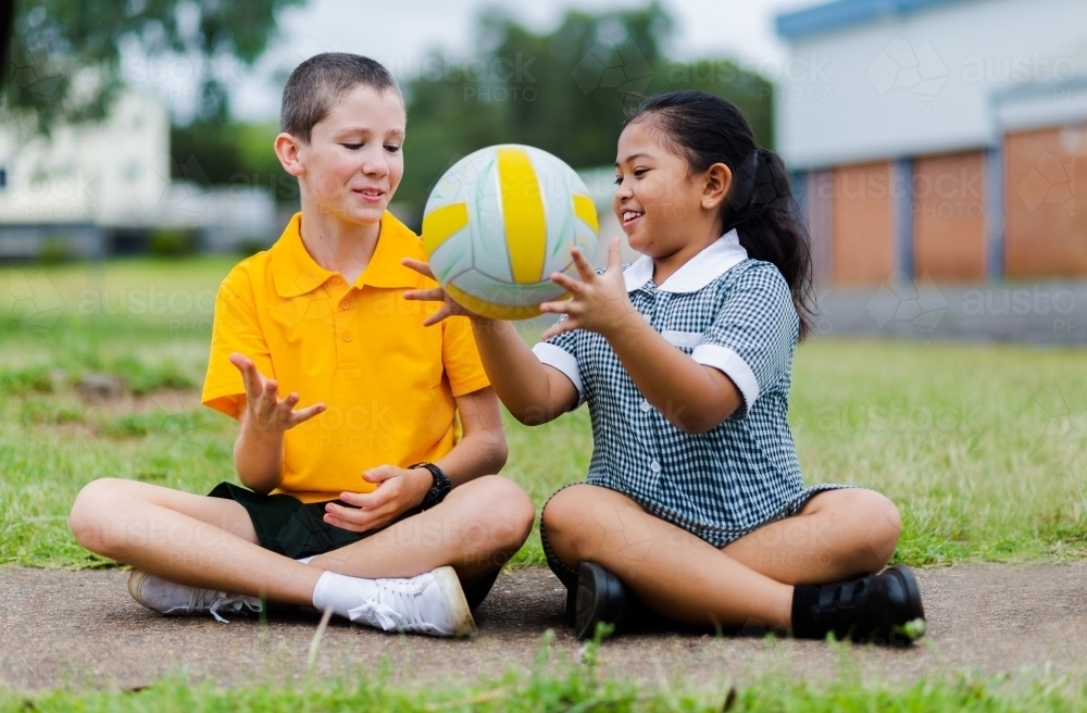 Aussie Boy and girl in playground at primary school throwing ball to each other - Australian Stock Image