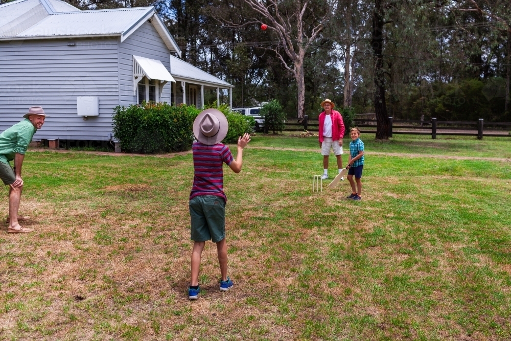 Aussie boys playing backyard cricket with their grandfather and dad in front yard - Australian Stock Image