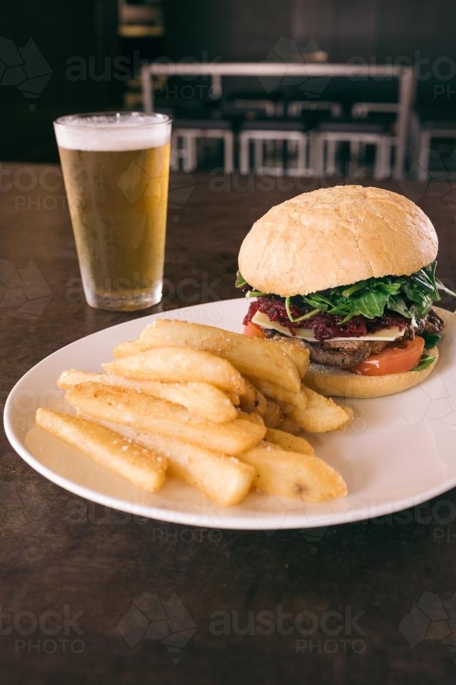 aussie burger with beetroot on plate with chips and a beer - Australian Stock Image