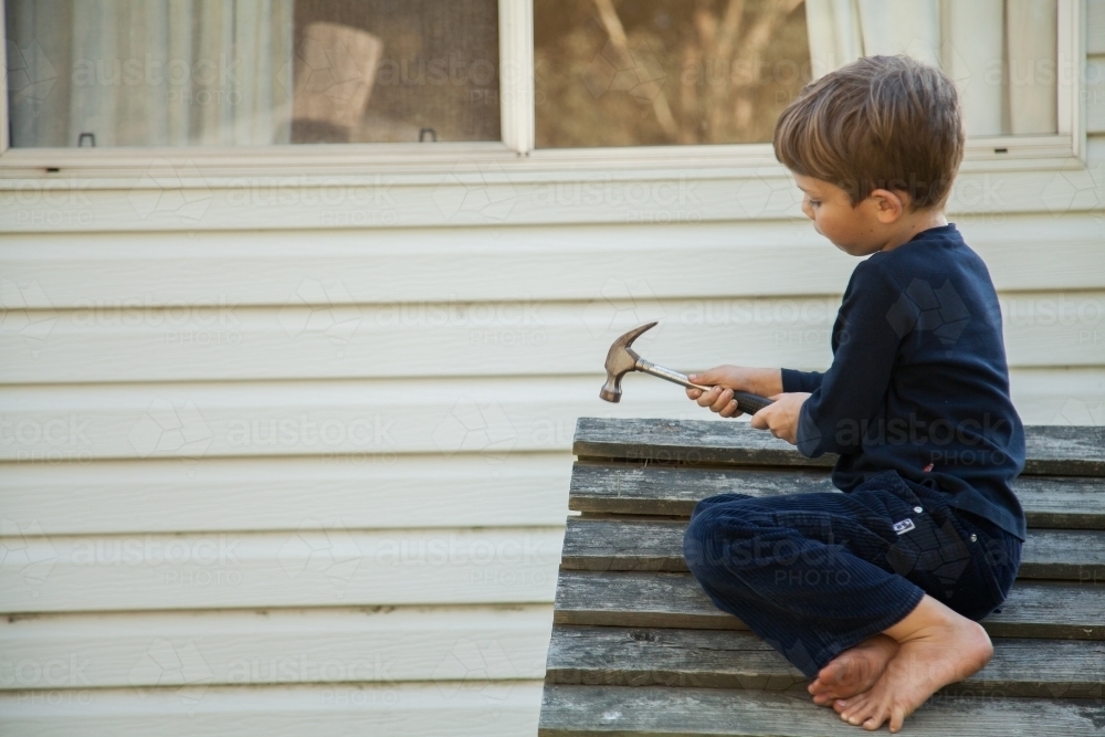 Aussie child hammering nails into roof of outside cubby house - Australian Stock Image