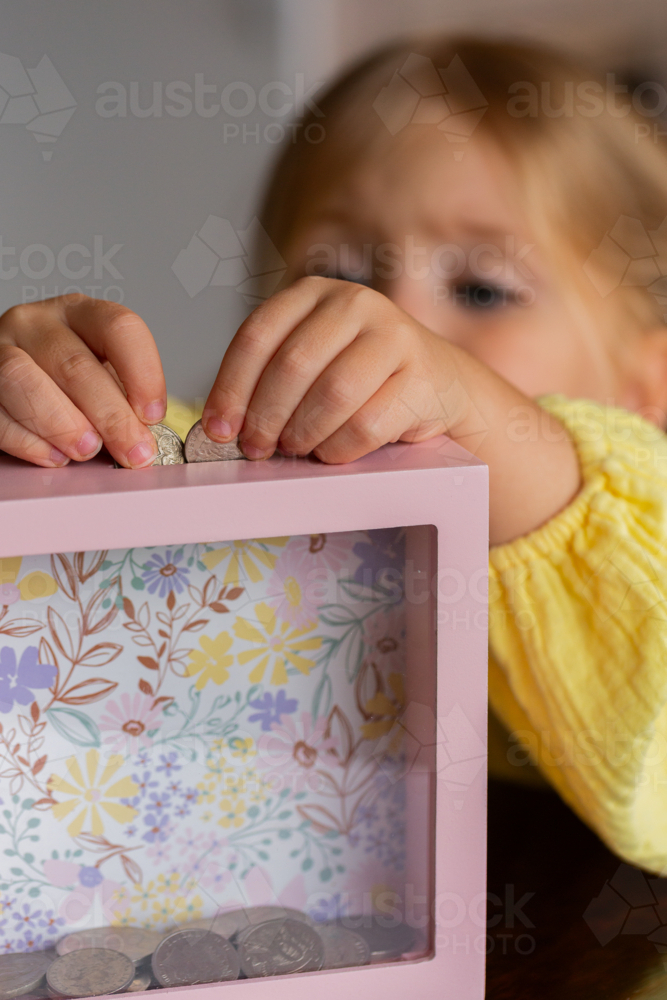 Aussie child putting Australian coins into moneybox at home - Australian Stock Image