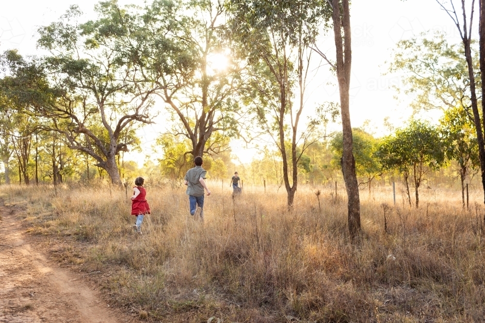 Aussie country kids running through dusty paddock in rural Australia - Australian Stock Image
