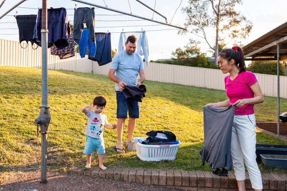 Aussie family getting in washing off clothesline in backyard together folding clothes - Australian Stock Image