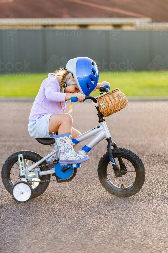 Aussie girl riding bike with training wheels on quiet suburban street - Australian Stock Image