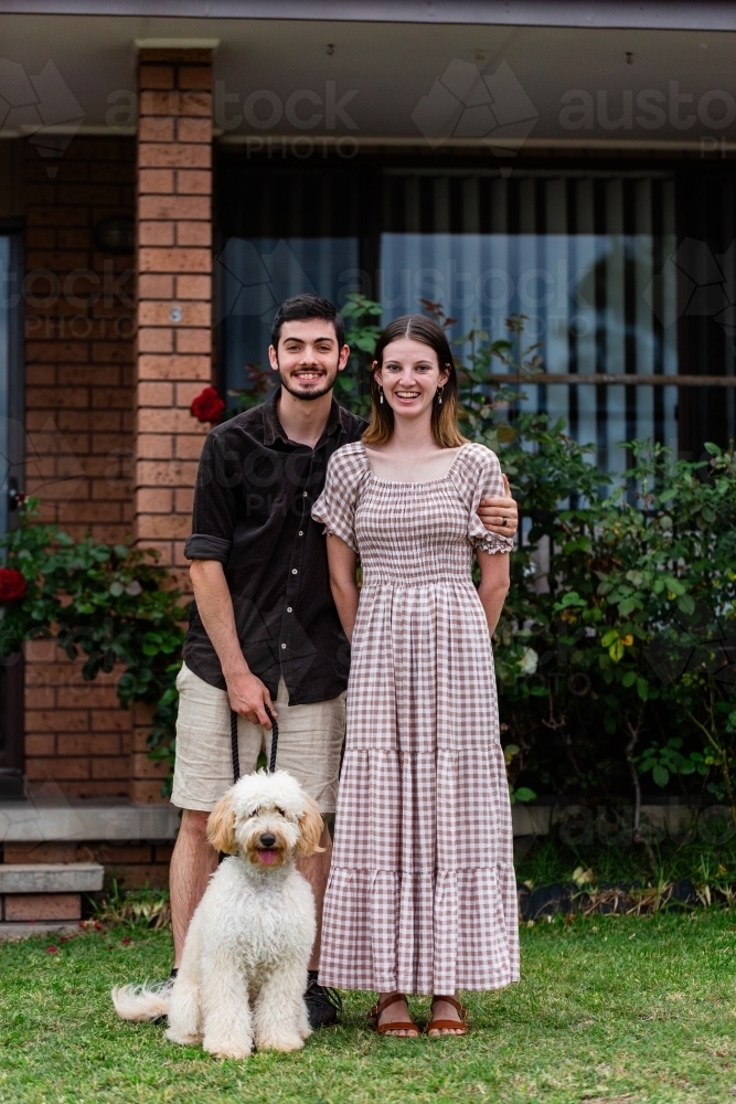 Aussie homeowner couple with pet tamaruke dog standing for portrait in front of home - Australian Stock Image