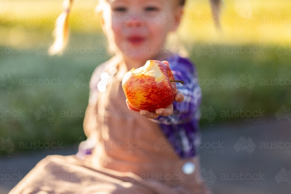 Aussie kid holding out fresh red apple with bite taken out of it - Australian Stock Image