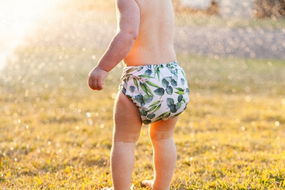 Aussie kid in cloth nappy playing in sprinkler water on a summer afternoon - Australian Stock Image