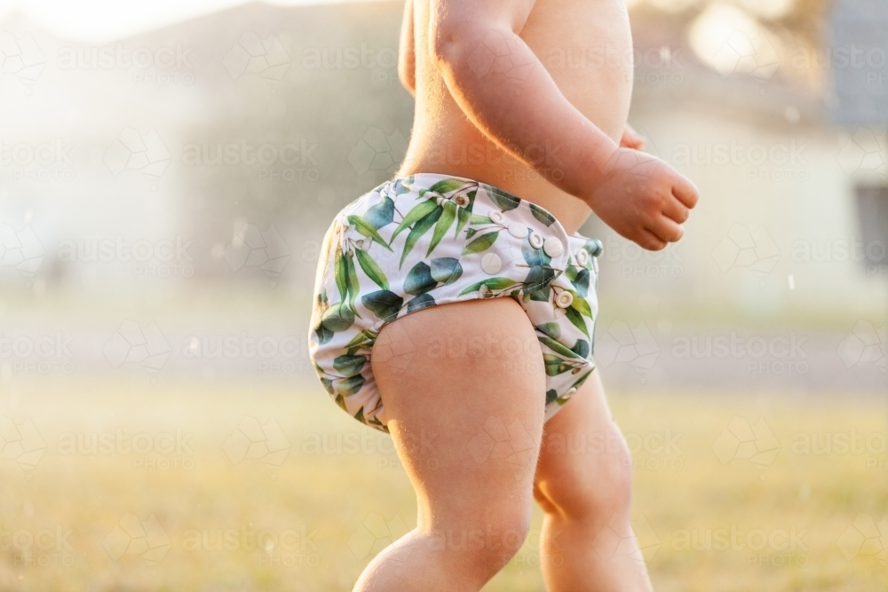 Aussie kid in cloth nappy playing in sprinkler water on a summer afternoon - Australian Stock Image
