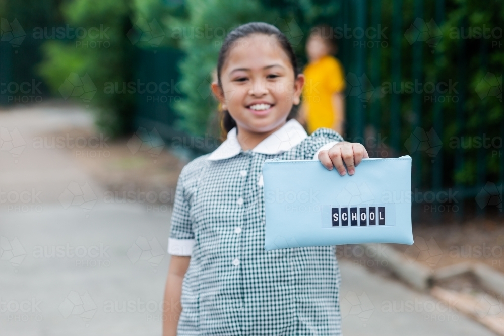 Aussie kid of Filipino ethnicity holding out a pencil case ready for going back to school - Australian Stock Image