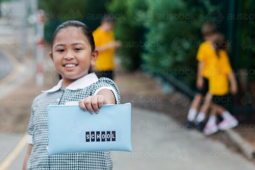 Aussie kid of Filipino ethnicity holding out a pencil case ready for going back to school - Australian Stock Image