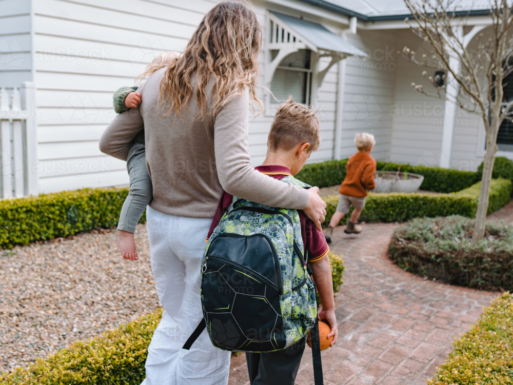 Aussie mum carrying toddler boy while walking with older son from school towards home - Australian Stock Image