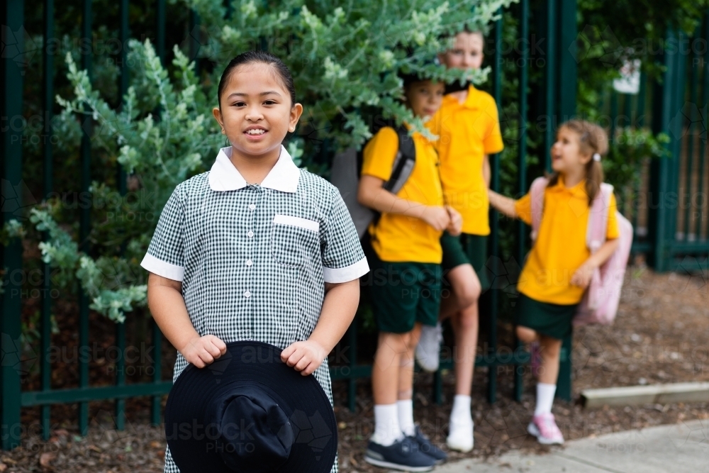 Aussie school girl holding her hat smiling with friends in background - Australian Stock Image