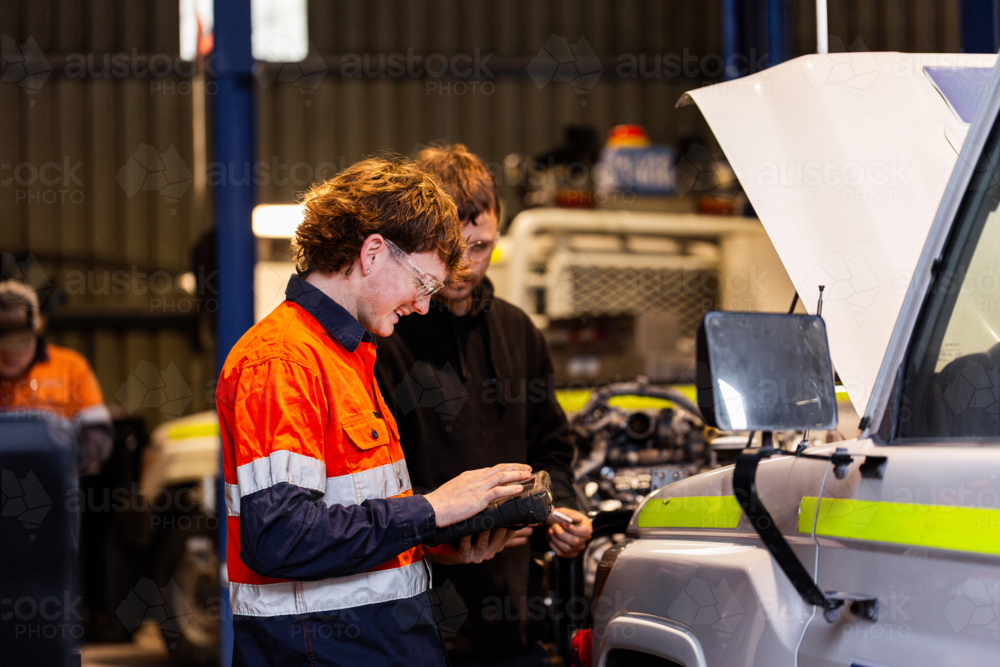 Aussie workman using digital diagnostics tool working on car vehicle engine in mechanics workshop - Australian Stock Image