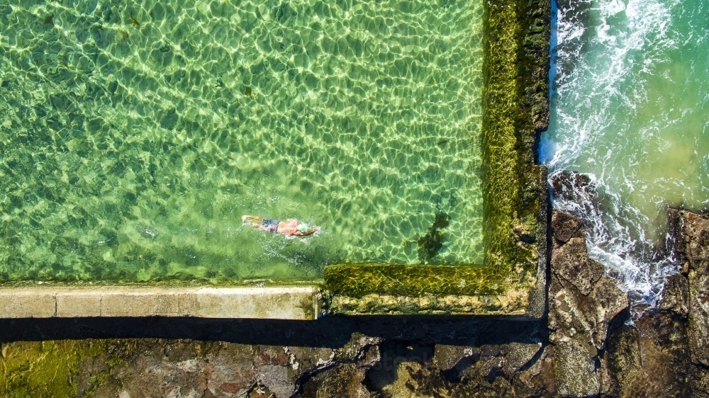 A mature man swimming laps in the Austinmer Rock Pool as waves lap the edges - Australian Stock Image