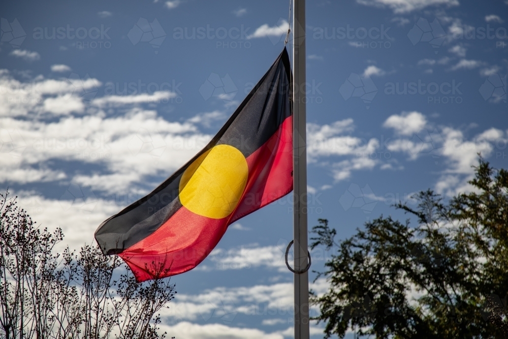 Australian Aboriginal flag flying in the wind with blue sky background - Australian Stock Image