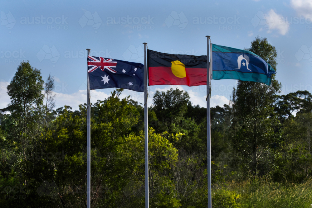 Australian, Aboriginal, Torres Strait Island flags flying on a sunny day with trees behind - Australian Stock Image