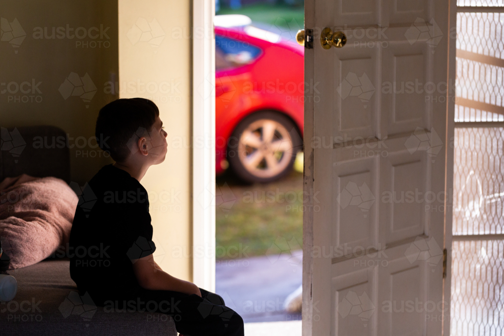 Australian boy sitting on lounge beside open door waiting - Australian Stock Image