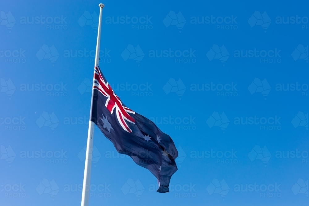 Australian Flag flown at half mast on a clear day with blue sky - Australian Stock Image