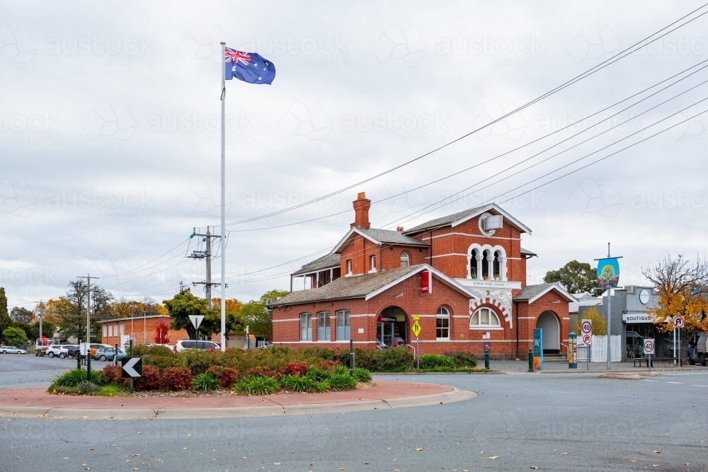 Australian flag flying on flagpole in country town of Euroa, with old historic post office building - Australian Stock Image