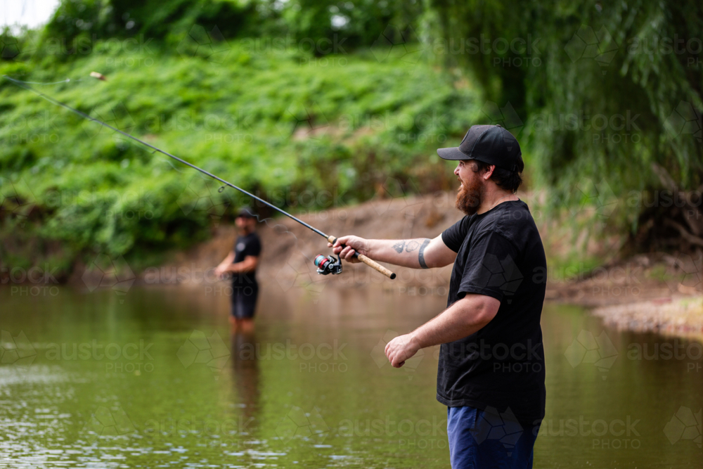 Australian men fishing together in river on summers day - Australian Stock Image