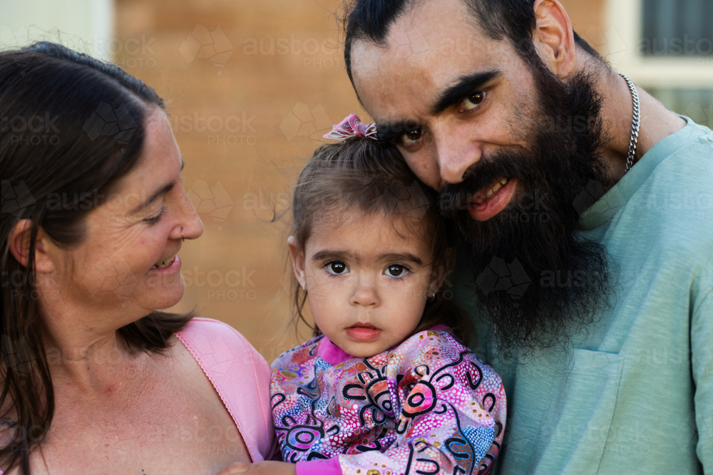 Australian parents with First Nations Australian toddler girl outside brick home - Australian Stock Image