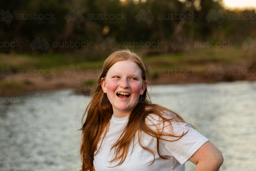 Australian redhead teen girl laughing beside river after sundown - Australian Stock Image