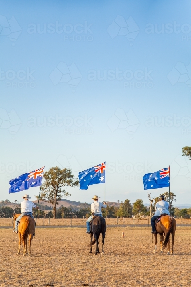 Australian stock horse riders holding flags while Advance Australia Fair national anthem is played - Australian Stock Image