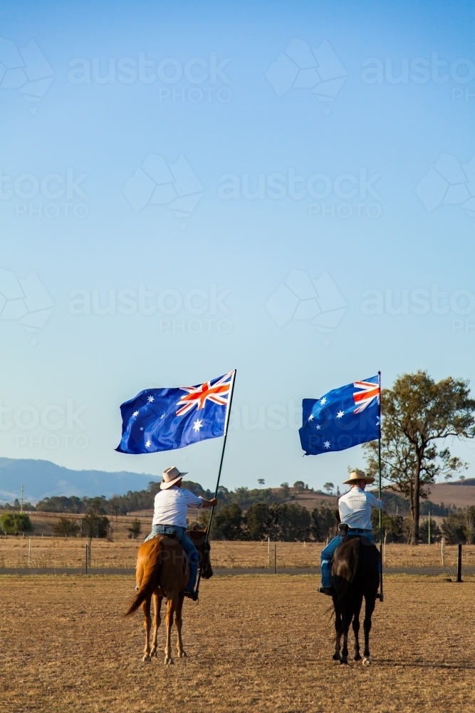 Australian stock horse riders holding flags while Advance Australia Fair national anthem is played - Australian Stock Image