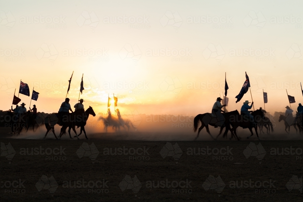 Australian Stock Horse riders riding in pairs silhouetted against dusty sunset - Australian Stock Image