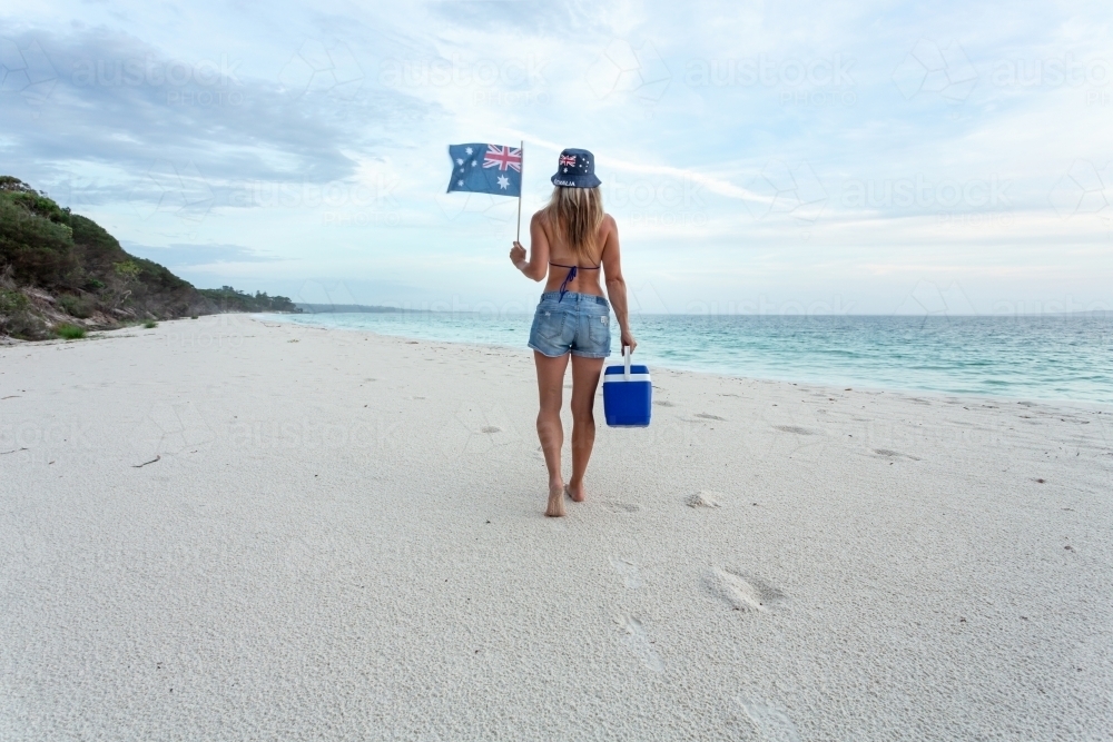 Australian woman in bikini and denim shorts walking along a beach with esky - Australian Stock Image
