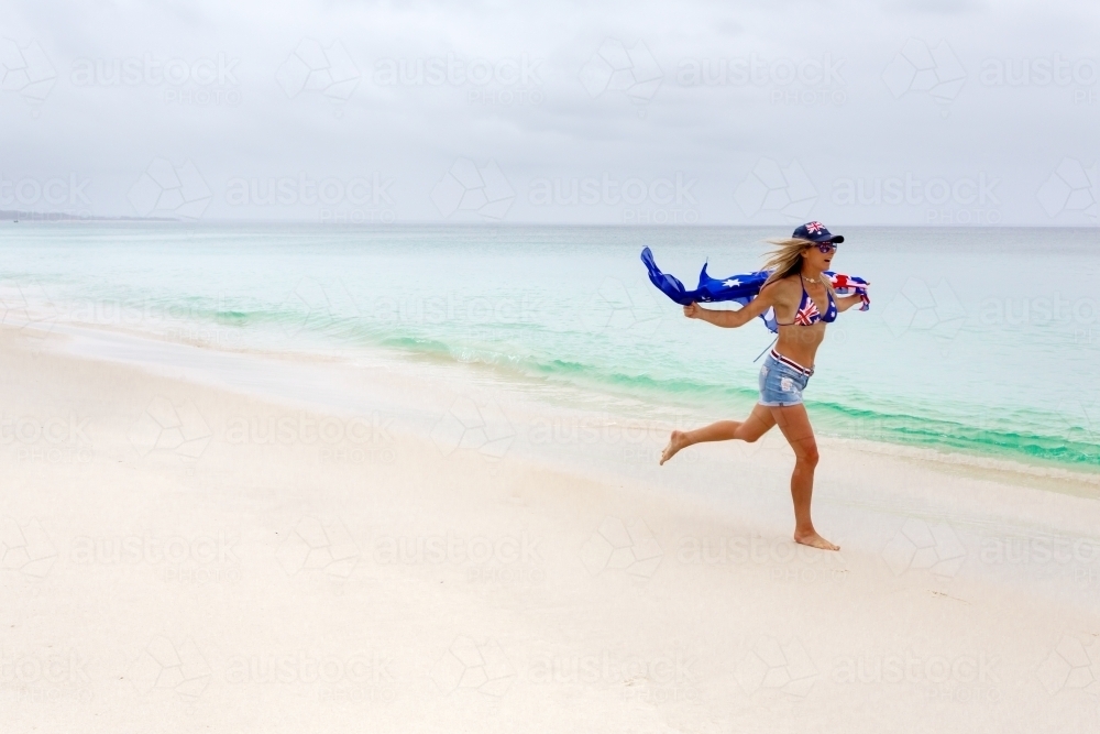 Australian woman running along the beach. She has the Australian flag printed on her cossie - Australian Stock Image