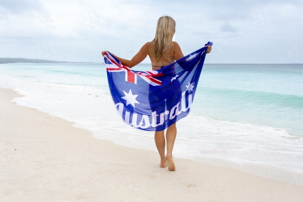 Australian woman walking along a beach waves washing up to her feet - Australian Stock Image