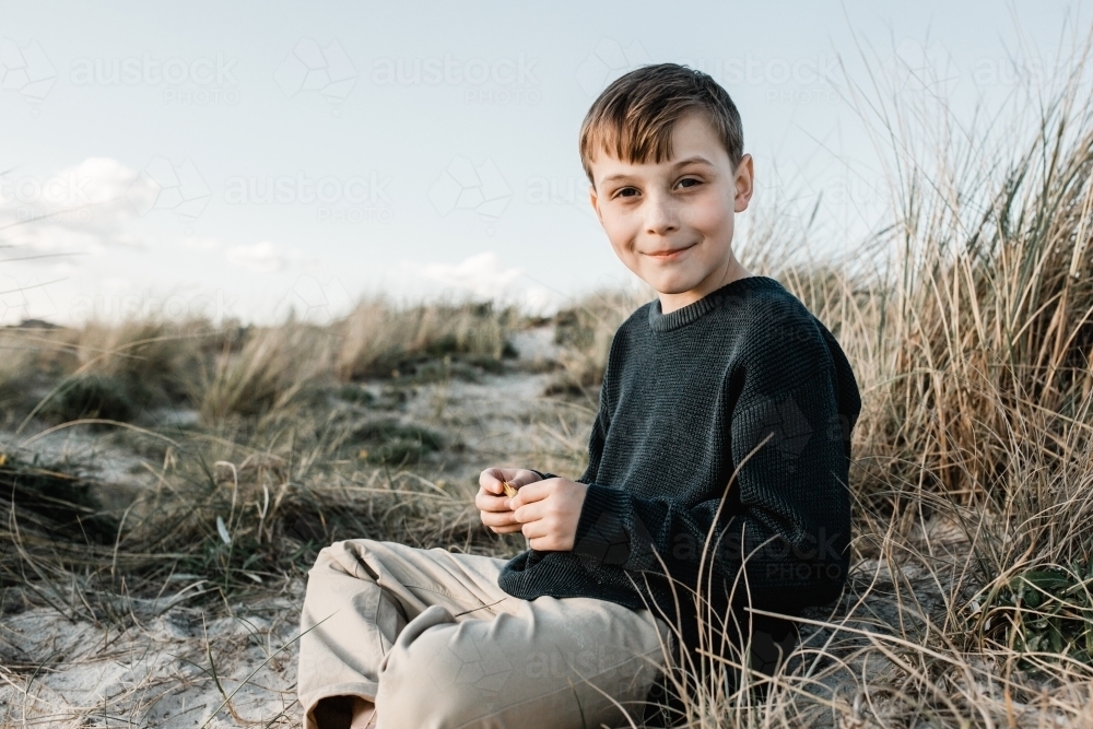 Autistic Boy sitting on a sand dune in the grass looking at the camera - Australian Stock Image