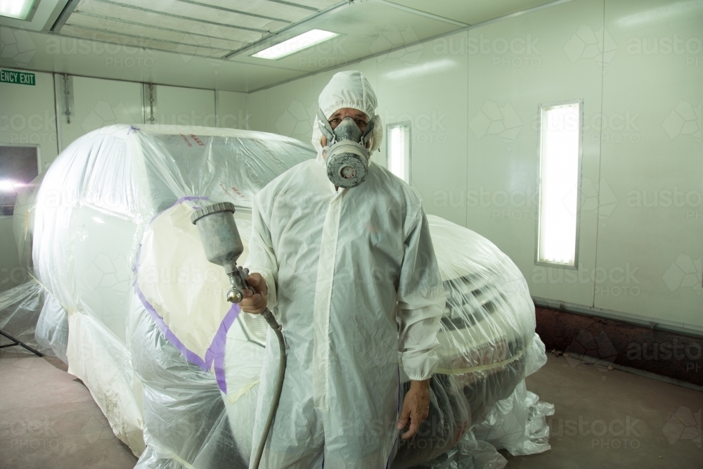 Image of Auto painter in protective suit and mask, spraying a car in