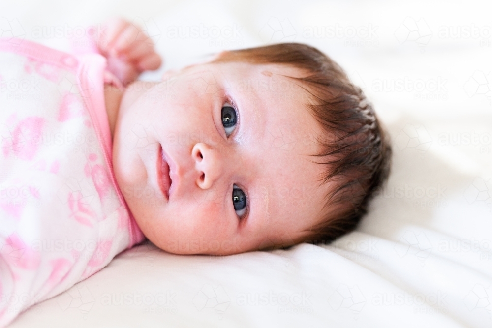 Awake little girl lying on white bed with wide eyes - Australian Stock Image