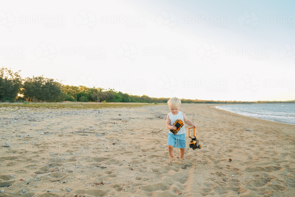 Baby boy carrying diggers along the sand at the beach : Austockphoto Baby boy carrying diggers along the sand at the beach - Australian Stock Image