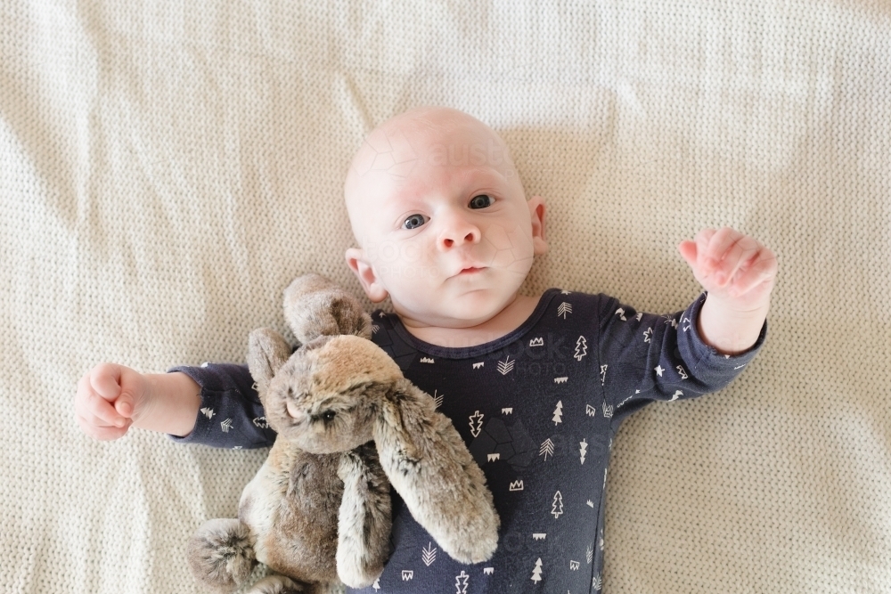 Baby boy looking at camera with soft toy rabbit - Australian Stock Image