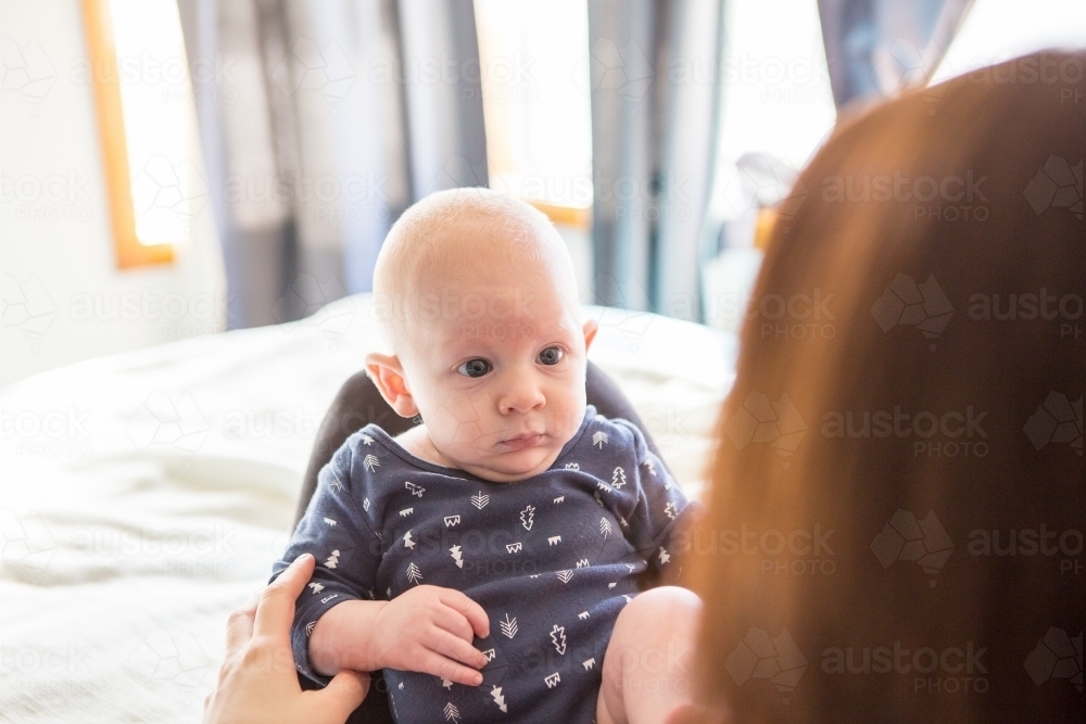 Baby boy on mothers knee looking at her - Australian Stock Image