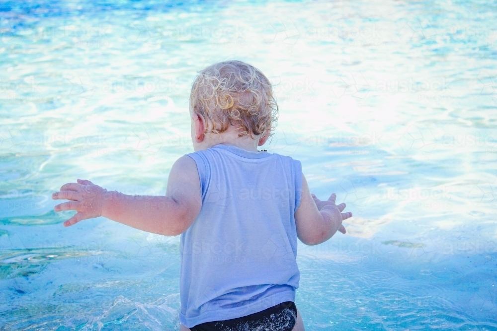 Baby boy standing at the edge of a sparkling blue resort swimming pool - Australian Stock Image