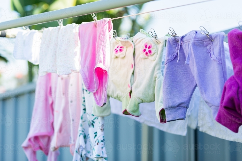 Baby clothes drying on clothesline pegged up with metal clothes pegs - Australian Stock Image