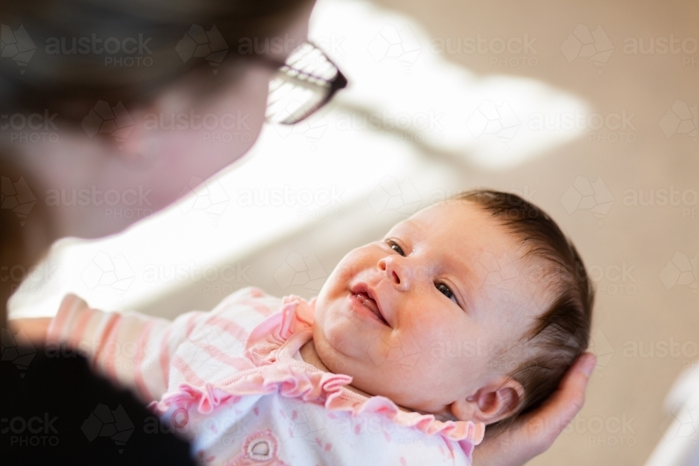baby girl being held by her young aunty smiling together inside home - Australian Stock Image