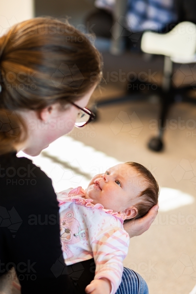 baby girl being held by her young aunty smiling together inside home - Australian Stock Image